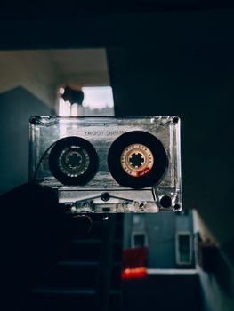 A vintage cassette tape held up in a stairwell with moody, dramatic lighting.