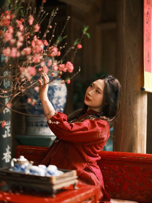 Free Beautiful woman in red dress admiring peach blossom indoors in Vietnam. Stock Photo