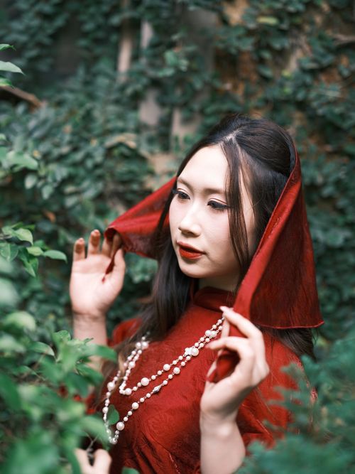Free A woman in red traditional attire poses gracefully surrounded by lush green foliage in Vietnam. Stock Photo