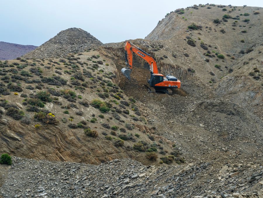 Excavator digging in rocky quarry terrain