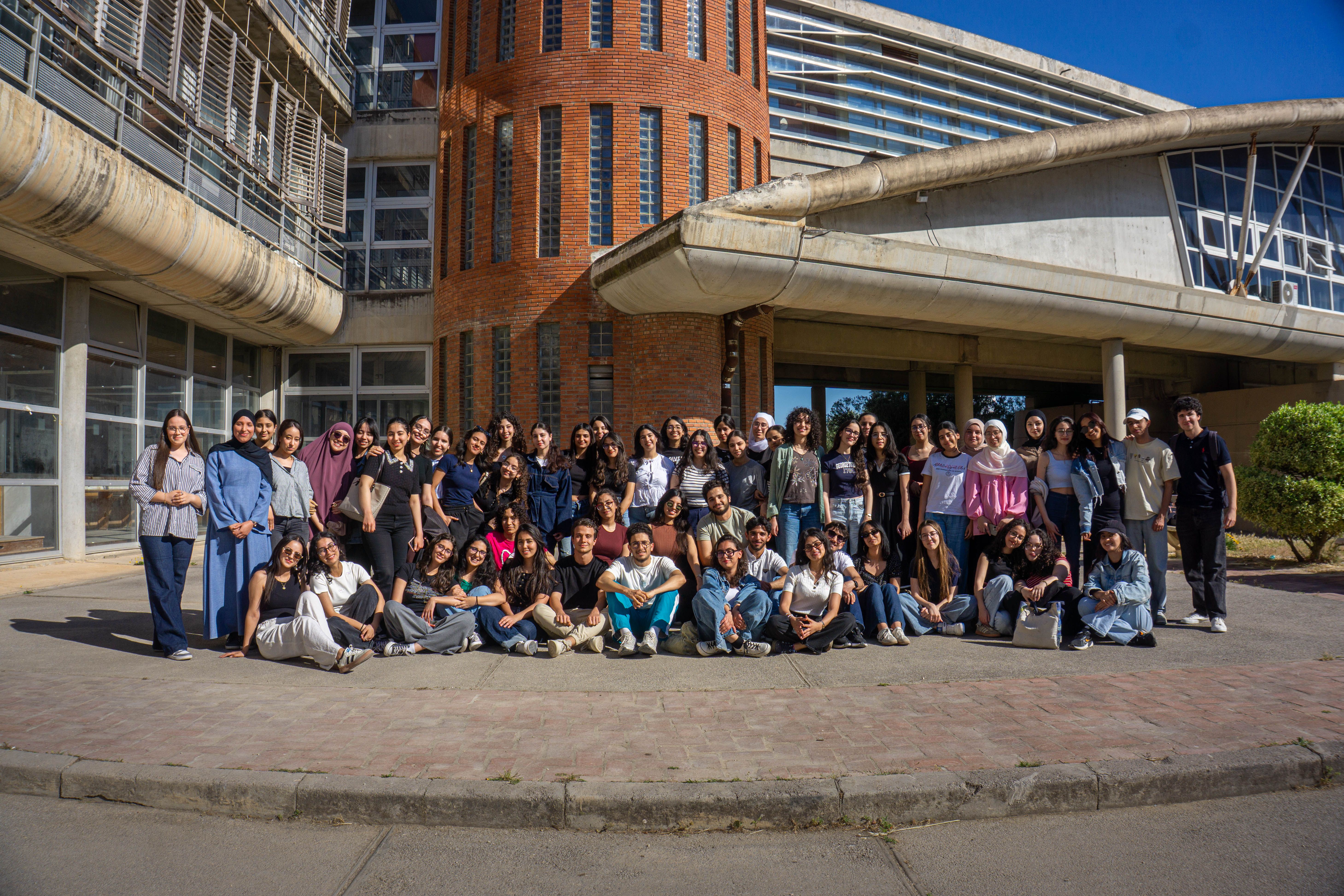 A diverse group of individuals gathered outside a modern architectural building for a group photo shoot.
