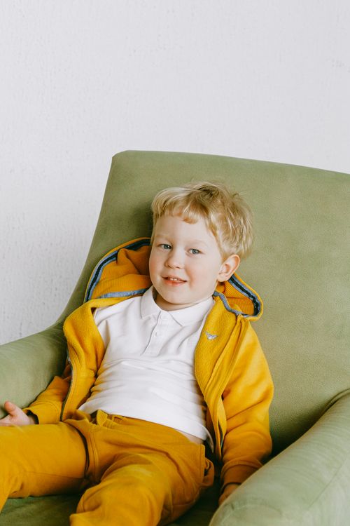 Free From above of cute smiling child in bright yellow tracksuit sitting in cozy armchair in living room  and looking at camera Stock Photo
