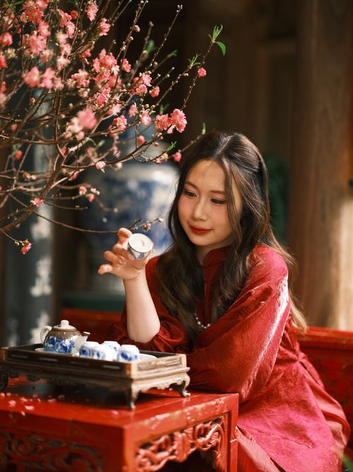 Free Woman in traditional Vietnamese attire savoring tea with cherry blossoms. Stock Photo