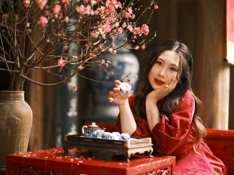 A woman enjoys a traditional Vietnamese tea ceremony beside cherry blossoms in a serene setting.