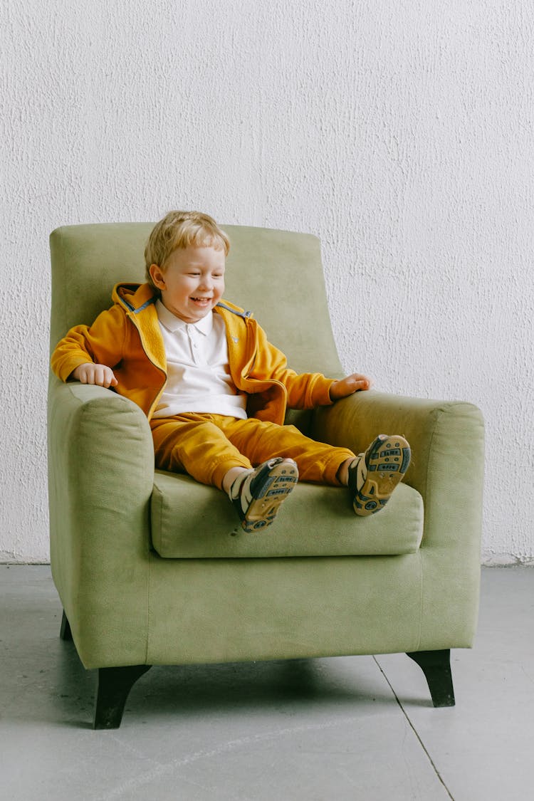 Smiling Little Boy Sitting In Armchair At Home