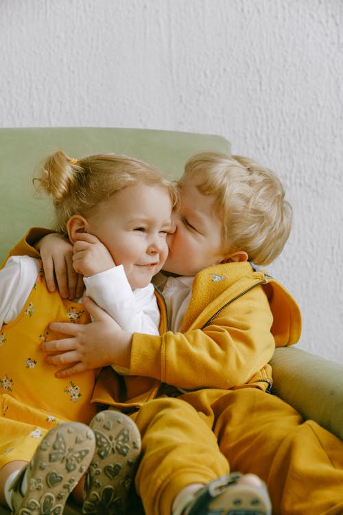 Cheerful little siblings hugging in armchair at home