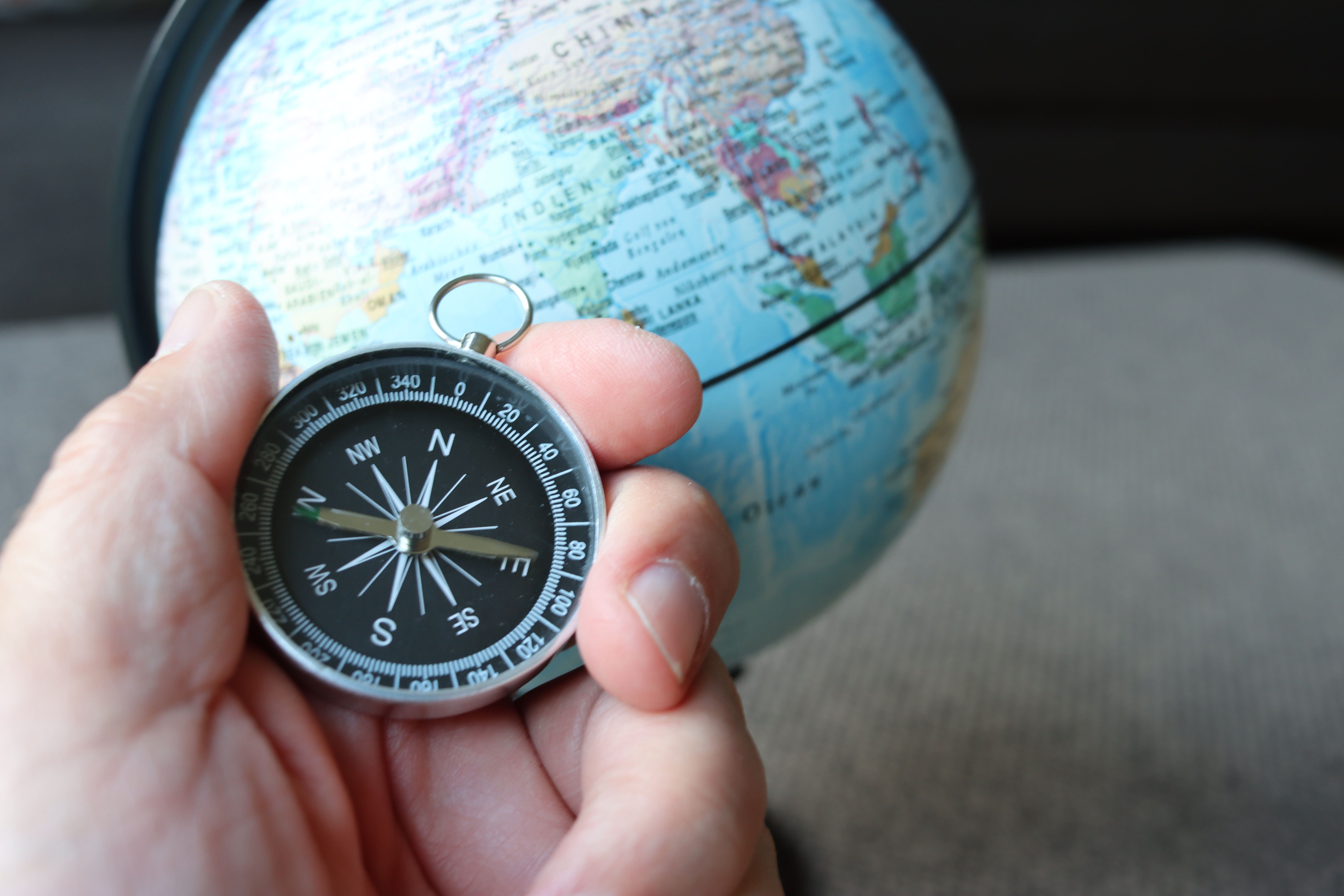 A hand holding a compass in front of a globe, symbolizing travel and navigation.