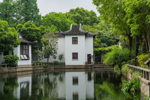 Free Tranquil view of traditional Chinese architecture surrounded by lush greenery reflecting on a calm pond. Stock Photo