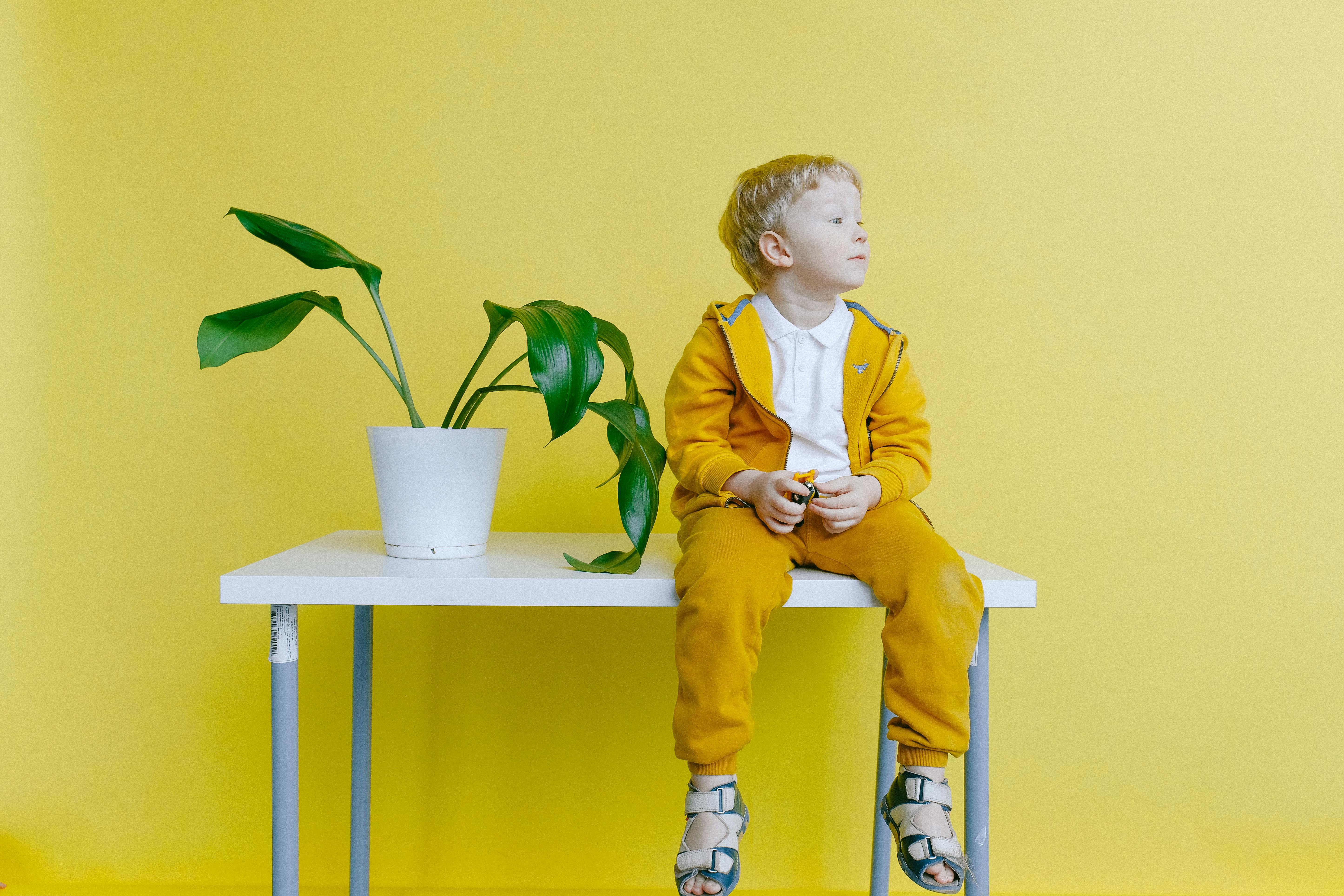 boy in yellow jacket and yellow pants sitting on white table