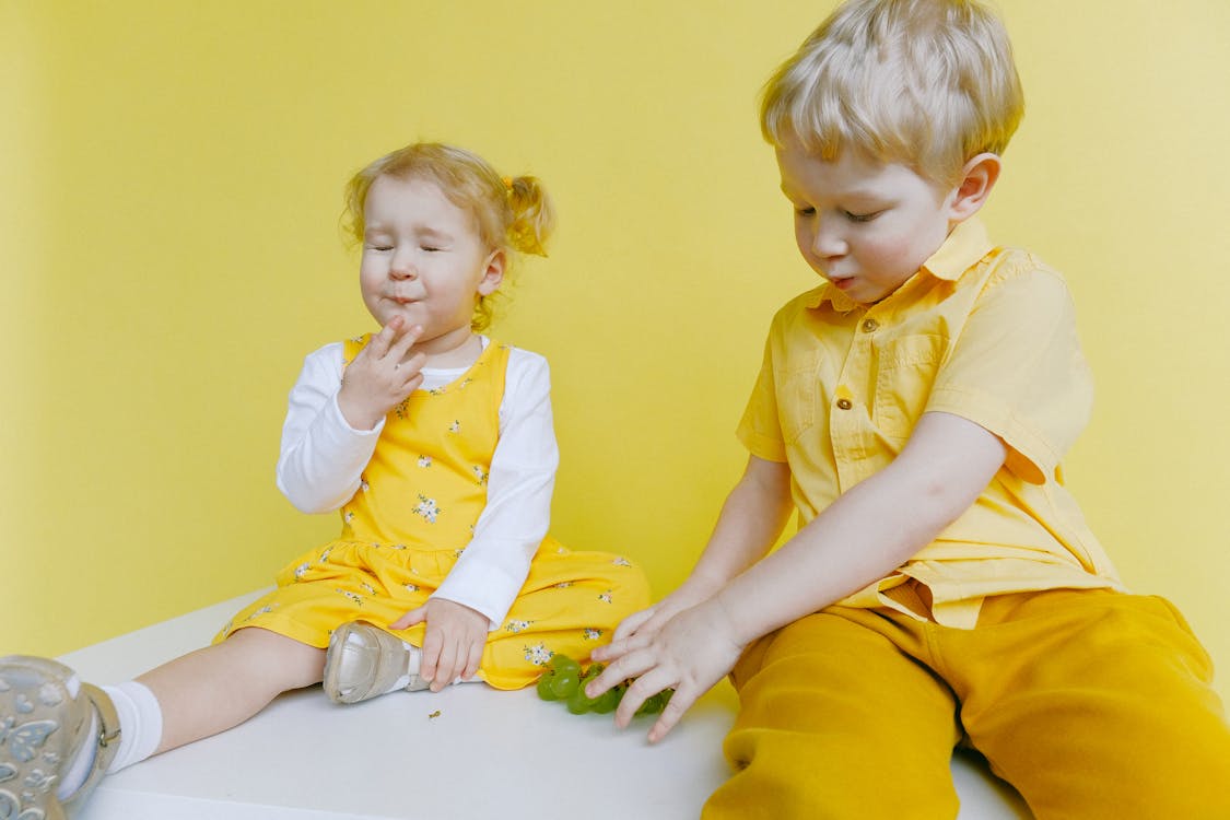 Toddlers Sitting On White Table While Eating Green Grapes 
