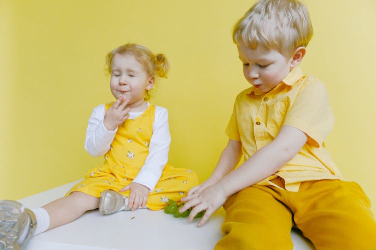 Toddlers Sitting On White Table While Eating Green Grapes