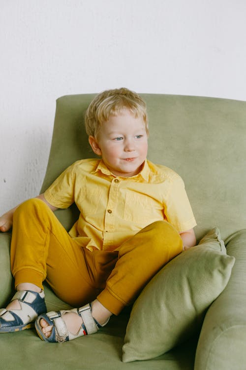 Jongen In Gele Knop Omhoog Shirt Zittend Op Grijze Bankstoel