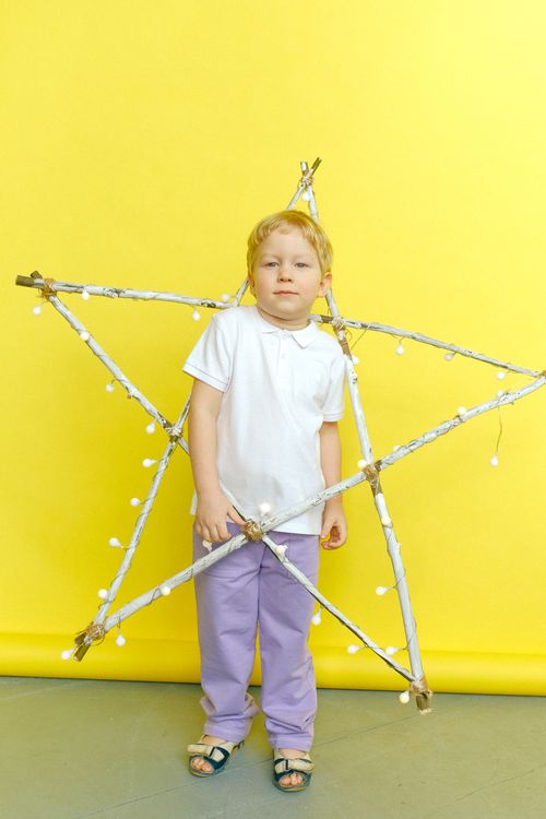 Free Young boy with blond hair posing with a star decoration in a studio on a bright yellow background. Stock Photo