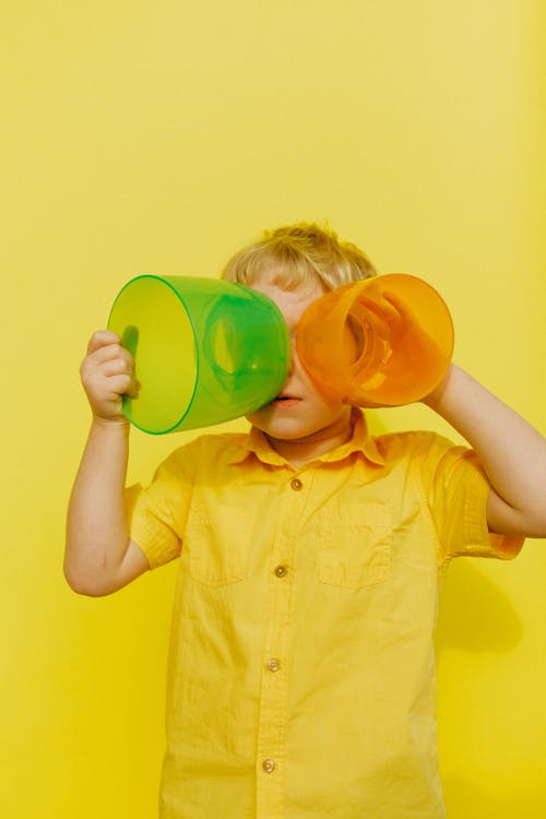 Мальчик в желтой рубашке на пуговицах с желтыми и зелеными пластиковыми контейнерами