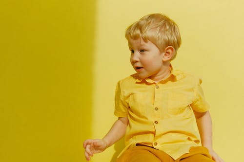Child in Yellow Button Up Shirt Sitting Near Wall