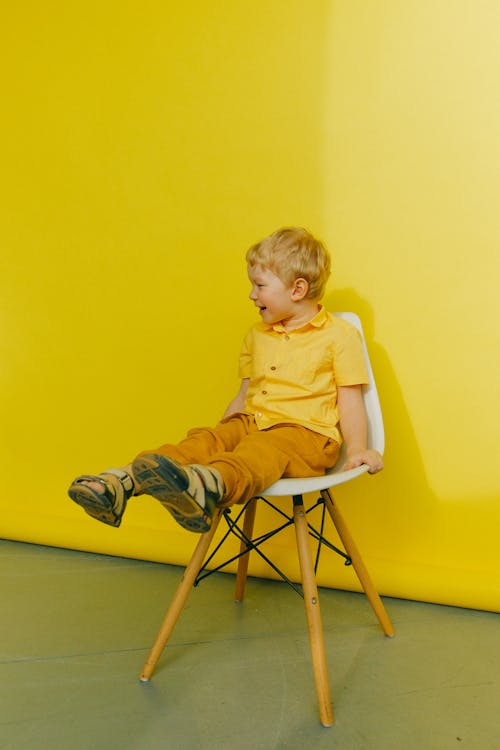 Boy in Yellow Polo Shirt Sitting on  Chair Near Wall