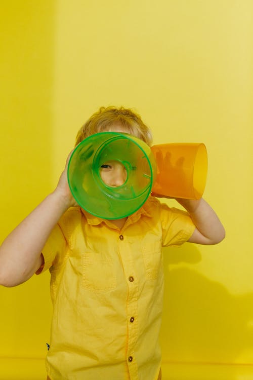 黃色按鈕的襯衫的男孩拿著綠色和橙色的塑料容器