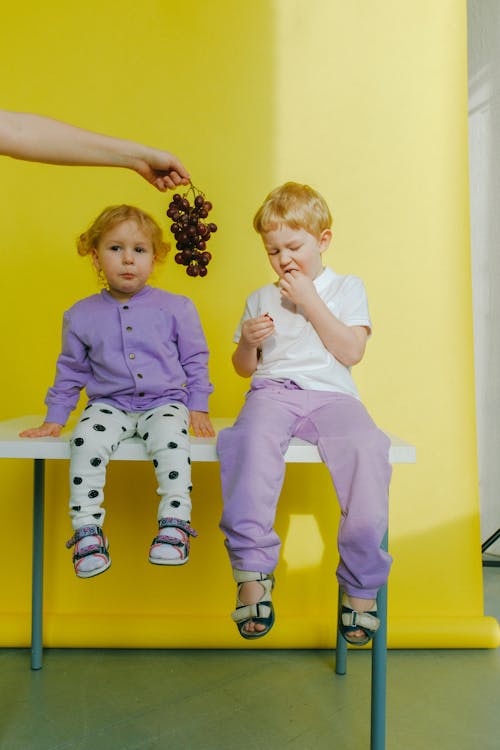 Person Holding Grapes Between Children Sitting on Table