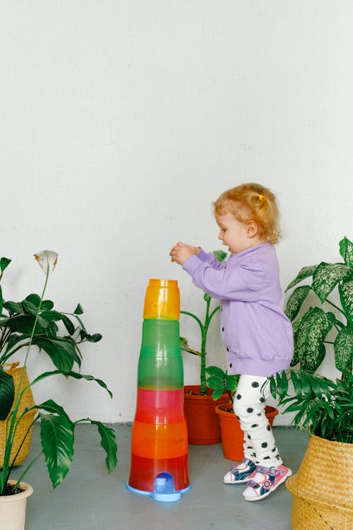 鉢植えの植物の横で遊ぶ紫色のセーターの女の子