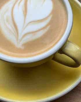 A beautifully crafted cappuccino with latte art served in a vibrant yellow cup and saucer.