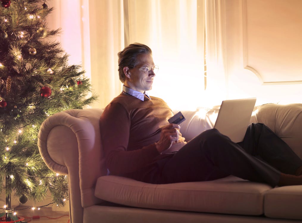 Free Man in Brown Long Sleeve Sweater and Black Pants Sitting on Brown Sofa Chair Using Laptop Stock Photo