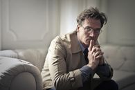 一个戴着眼镜的男人若有所思地坐在光线充足的房间里的沙发上