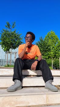 Casual portrait of a man in an orange shirt sitting outdoors, exuding a thoughtful vibe.