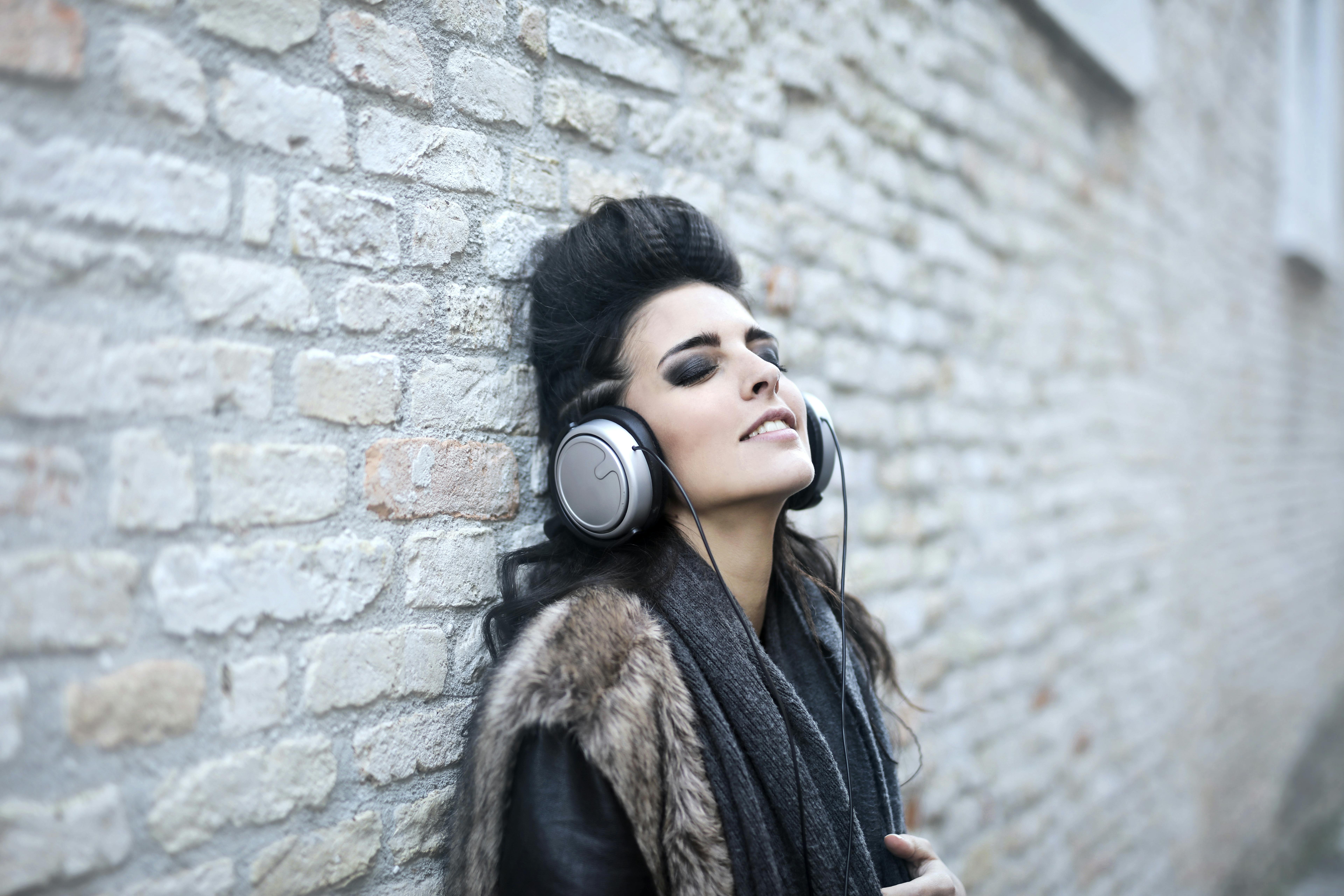 informal young woman listening to music near grunge wall