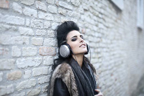 Free Informal young woman listening to music near grunge wall Stock Photo