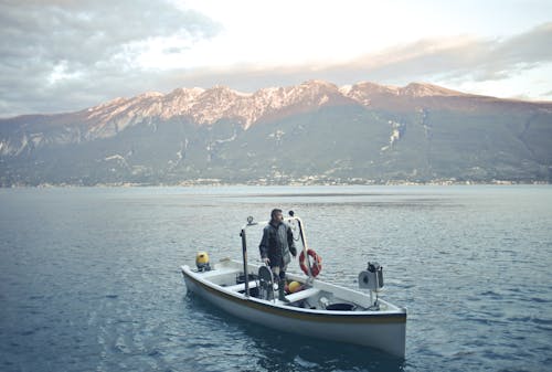 Man in Black Jacket Standing on White and Black Boat on Sea