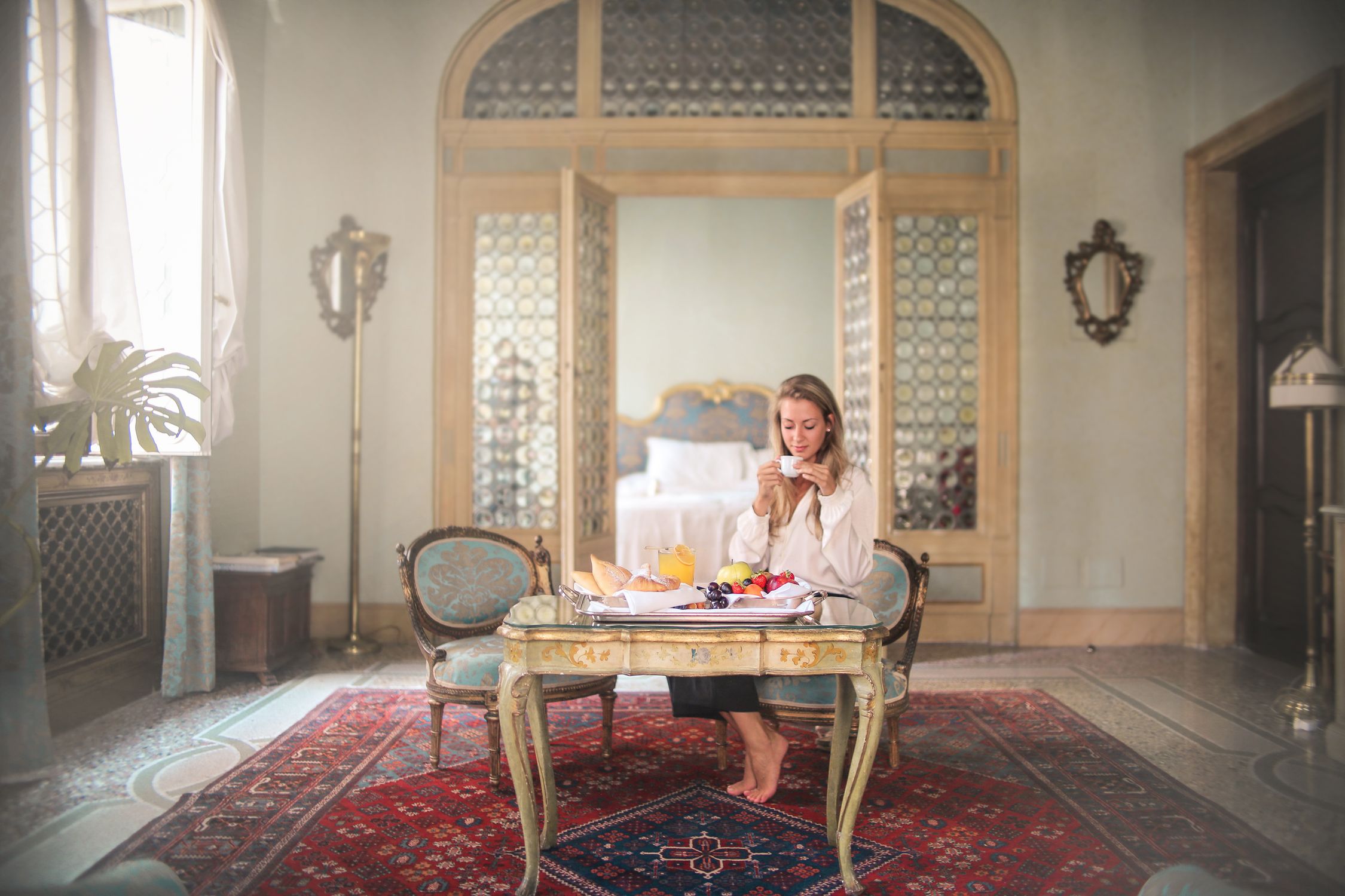 Full body chilling woman sitting in spacious living room of luxurious hotel room having healthy breakfast and drinking coffe