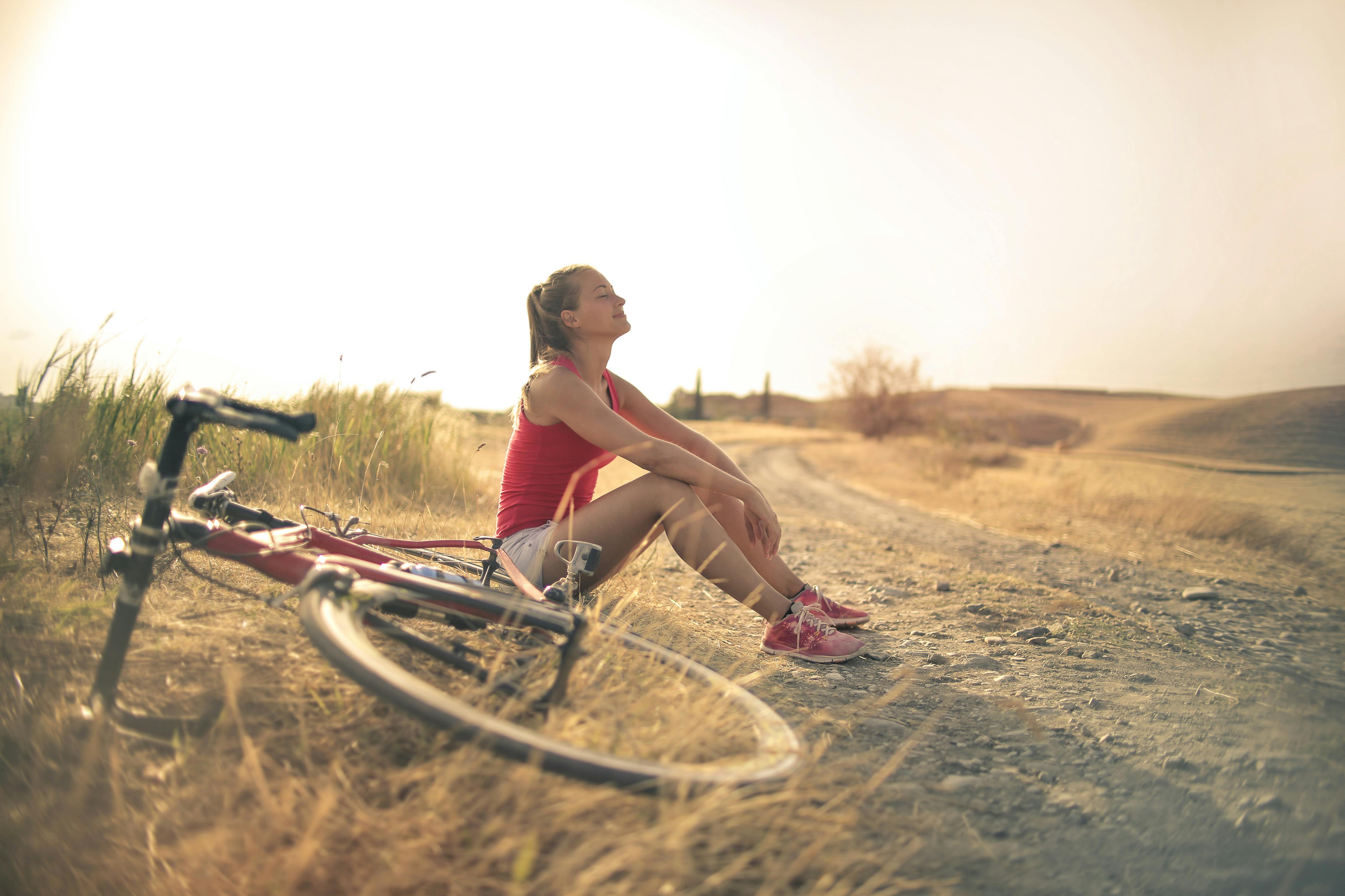 Sportive woman with bicycle resting on countryside road in sunlight