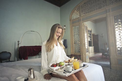 有早餐的快樂的婦女在旅館臥室的盤子