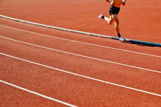 Athlete running on a red track in an outdoor stadium on a sunny day.