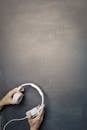 From above of hands of male with white modern headphones on background of shabby chalkboard