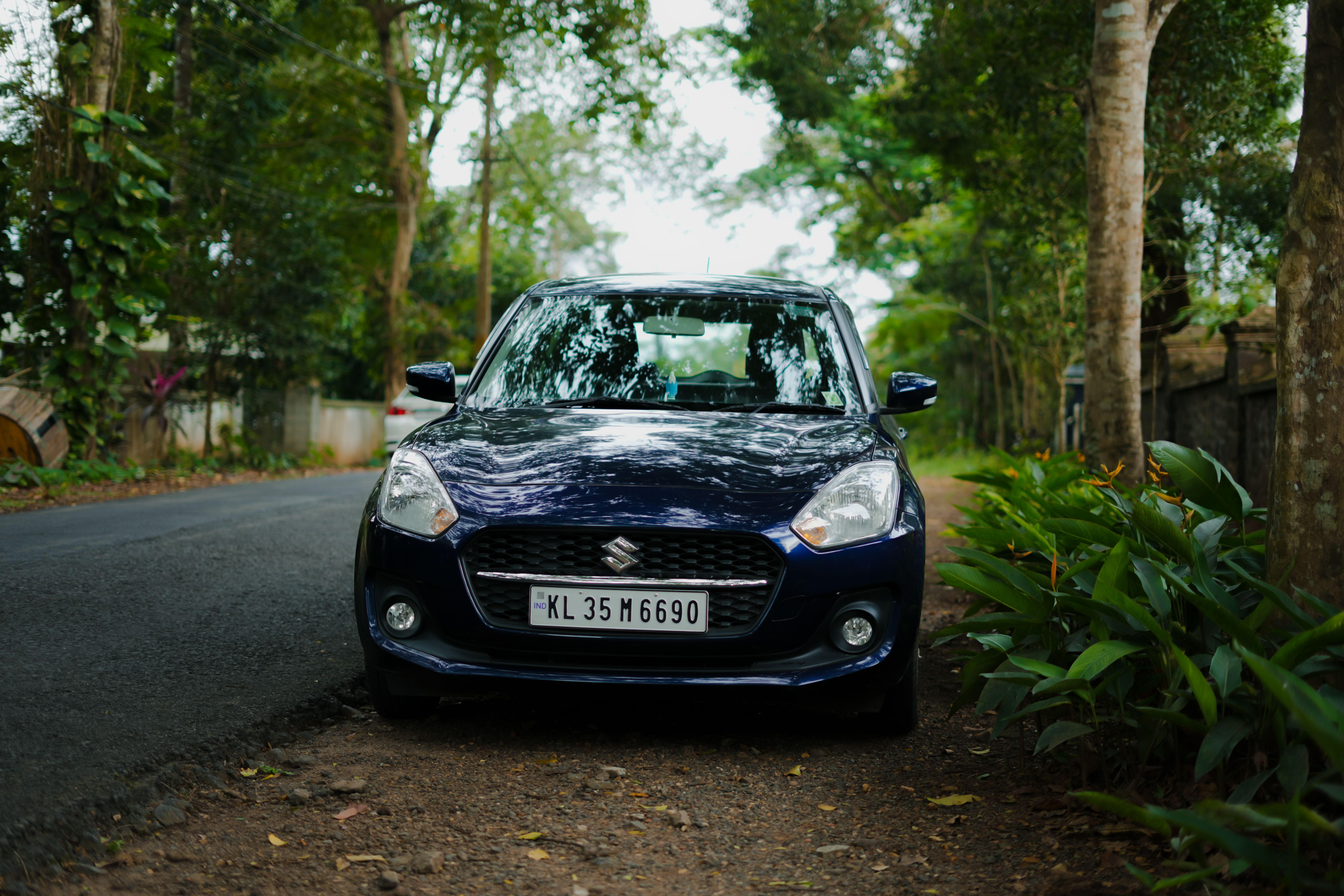 A black compact car parked on a scenic, tree-lined roadside in KL, India.