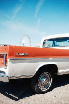 Vintage pickup truck parked near a Ferris wheel on a bright sunny day, evoking nostalgia.