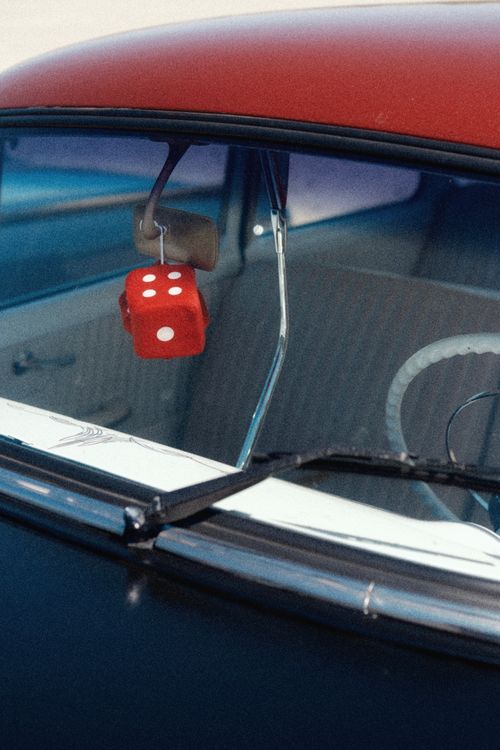 Free Close-up of a classic car's interior featuring red fuzzy dice hanging from the rearview mirror. Stock Photo