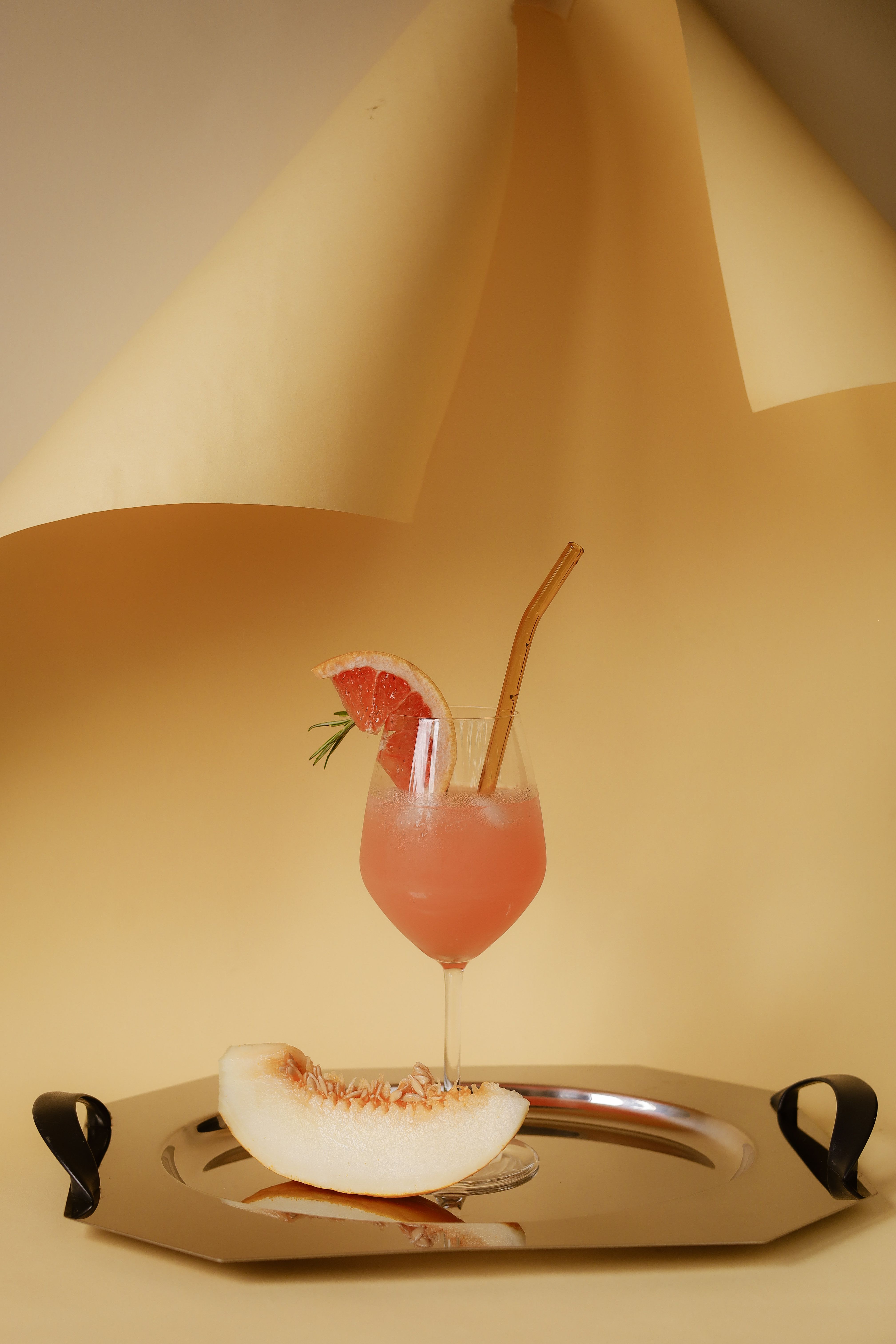 Chic pink grapefruit cocktail on tray with melon slice, perfect for summer refreshment.