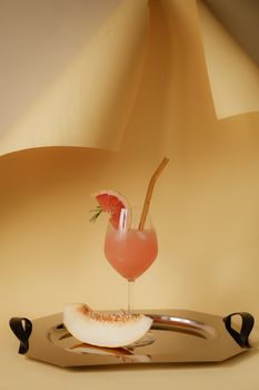 Chic pink grapefruit cocktail on tray with melon slice, perfect for summer refreshment.