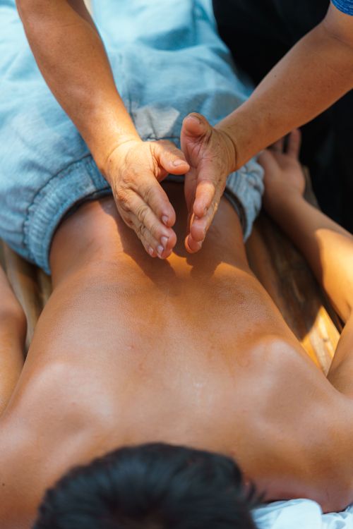 Free A therapist performs a soothing massage on a person's back under natural sunlight, promoting relaxation. Stock Photo