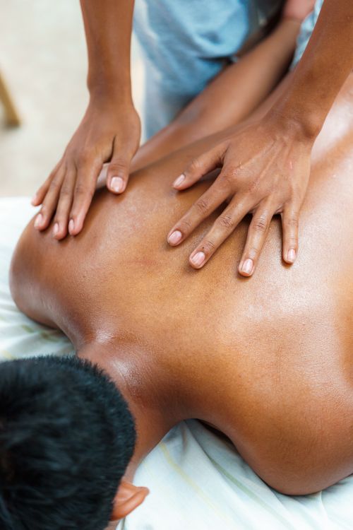 Free Therapist giving a professional massage to a client lying face-down indoors. Stock Photo