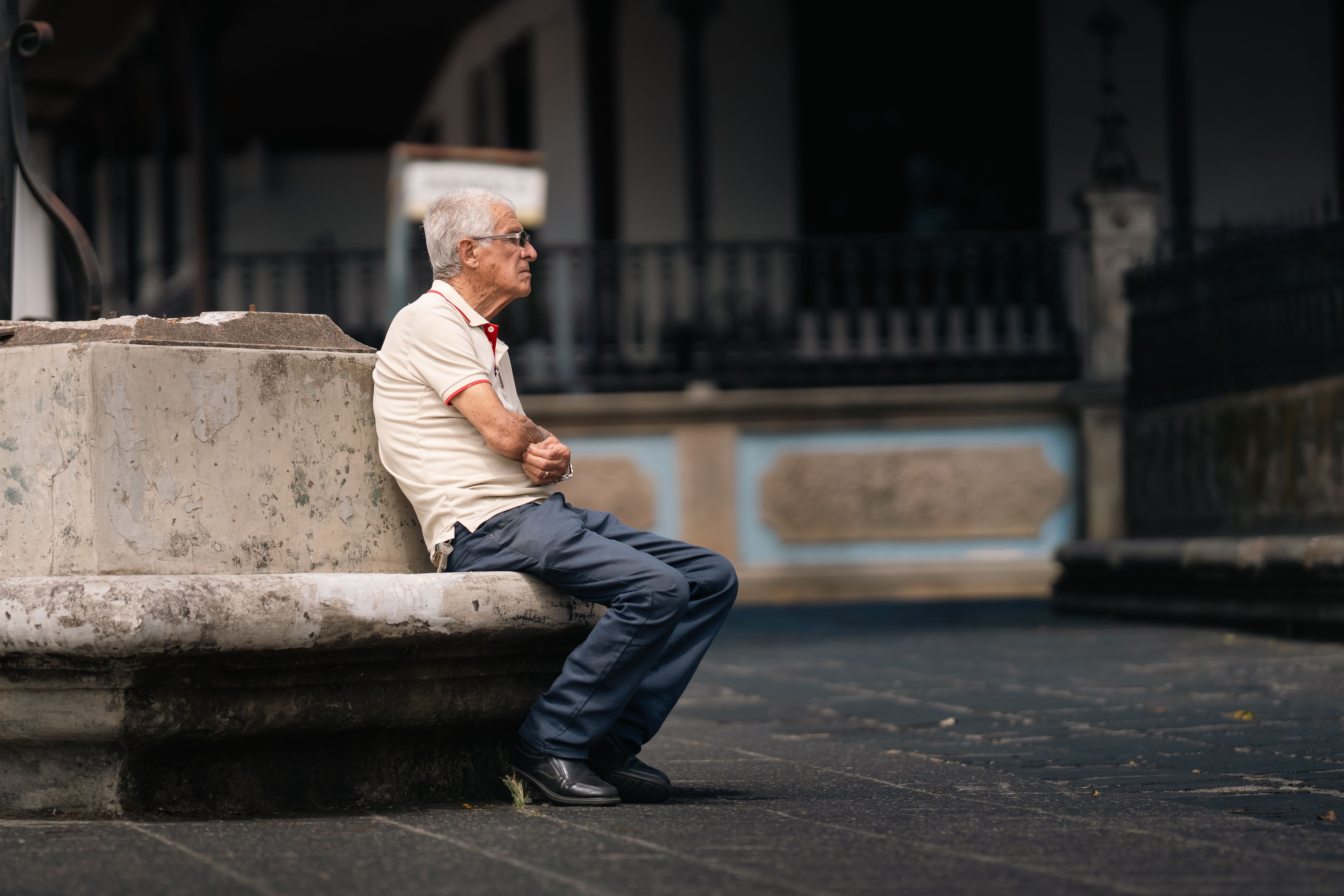A senior adult sitting contemplatively on a stone bench in San José, Costa Rica.