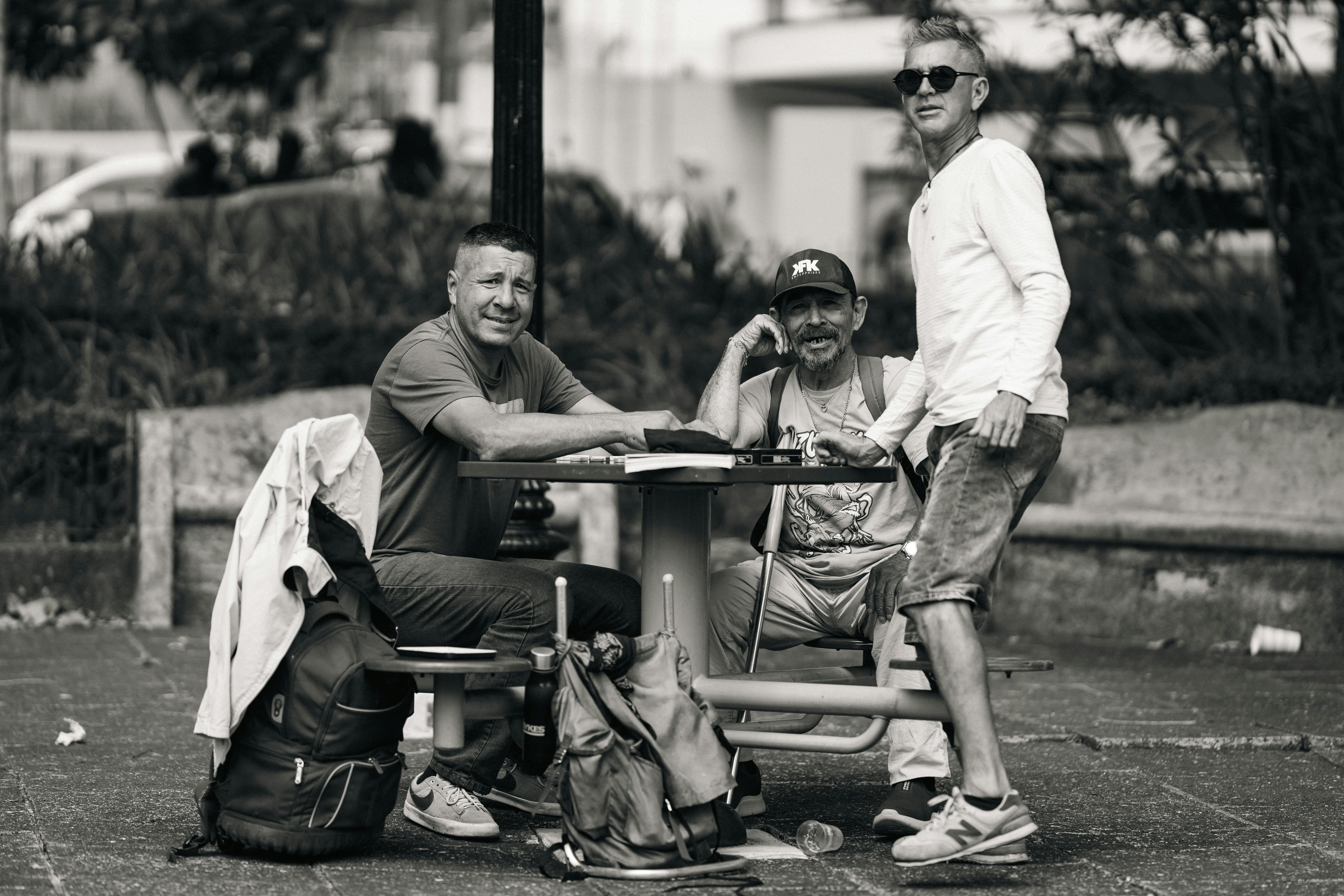 A candid black and white photo of three men chatting at a park table in San José, Costa Rica.