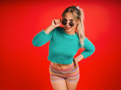Trendy young woman in sunglasses poses confidently against a vibrant red background.