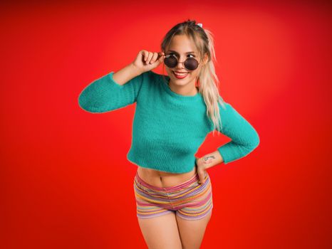 Smiling young woman in colorful outfit striking a playful pose against a bright red background.
