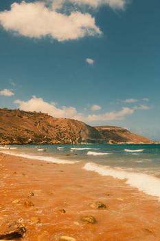 Explore a serene golden sand beach with rolling waves under a bright blue sky.