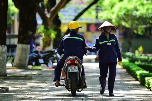 Free Two workers interact on a motorbike in a lush city park, highlighting urban daily life. Stock Photo