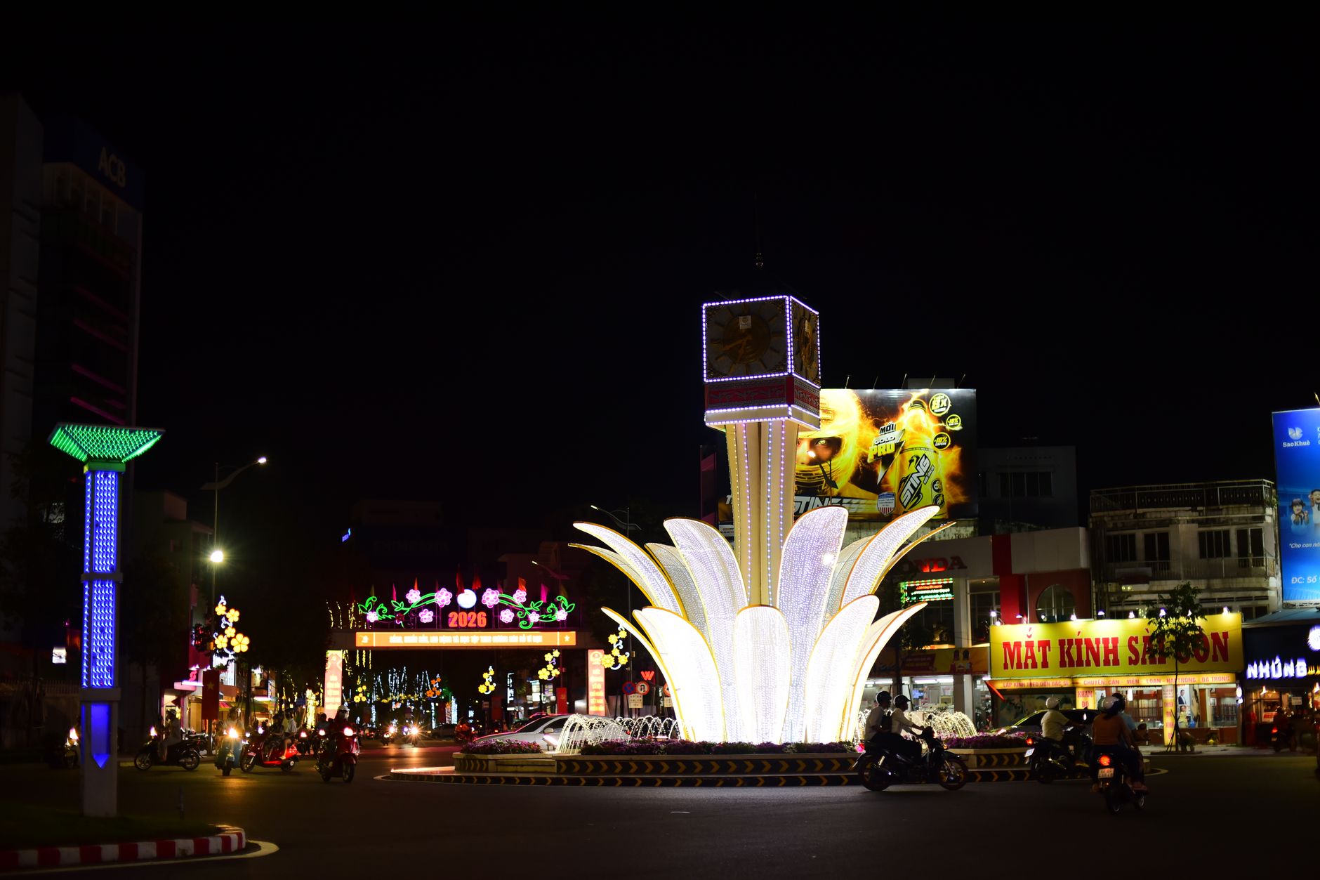 A vibrant illuminated fountain in an urban cityscape at night with busy street traffic and neon signs.