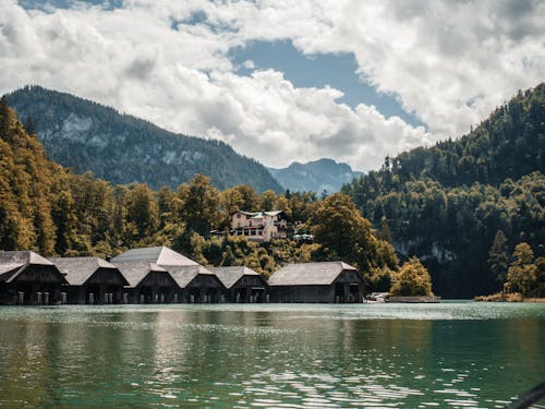 Boathouses on Lake Near Green Trees Under White Clouds and Blue Sky